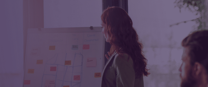 A woman working in people analytics is utilizing her data to gain valuable insights from a white board with post it notes. She is discussing these insights with her team. There is a purpleish blue gradient layered over the image, indicating the post is from Crunchr