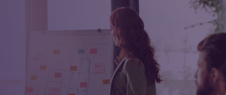A woman working in people analytics is utilizing her data to gain valuable insights from a white board with post it notes. She is discussing these insights with her team. There is a purpleish blue gradient layered over the image, indicating the post is from Crunchr